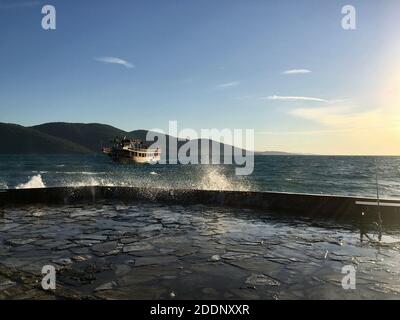 Tour Boot auf Wellenwasser mit nasser Küste. Großer großer Sturm wie Wellen mit offenem klaren blauen Himmel und wenigen Wolken, sonniger Tag. Stockfoto