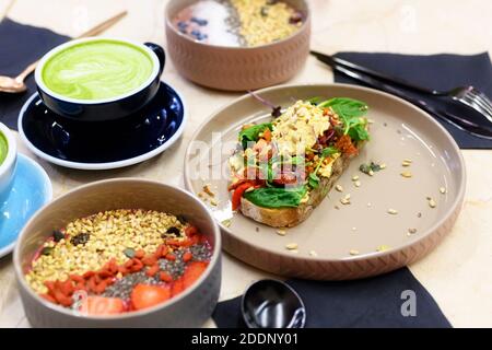 Rohkost gesundes Frühstück. Smoothie Schüssel, Toast mit Hummus und Matcha Latte grünen Tee Tasse auf dem Tisch Stockfoto