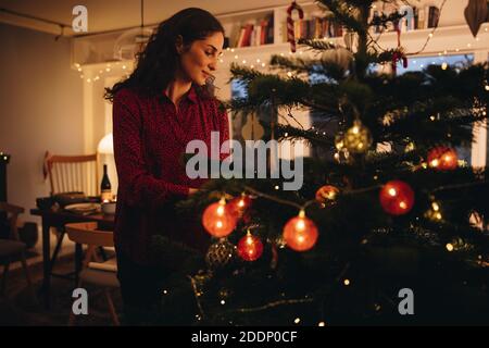 Frau Dekoration Weihnachtsbaum allein zu Hause. Weibliche hängende Ornamente auf einem weihnachtsbaum in Familie zu Hause. Stockfoto