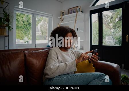 Glückliche Frau entspannen auf bequeme Couch mit Smartphone-Browsing Social Medien Stockfoto