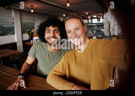 Portrait von lächelndem jungen Paar, das sich im Café entspannt und Selfie nimmt Im Mobiltelefon Stockfoto