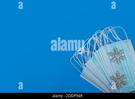 Blaue Schutzmasken mit silbernen Schneeflocken auf blauem Hintergrund. Coronavirus-Schutz. Weihnachts- und BEW-Jahreskonzept. Flach liegend. Speicherplatz kopieren Stockfoto