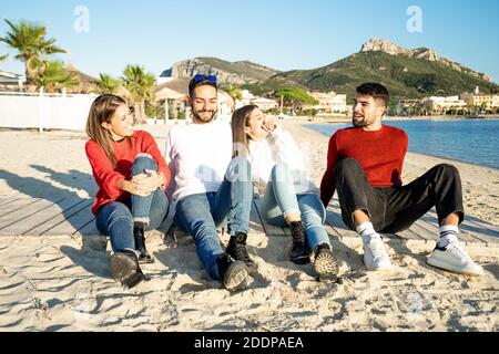 Zwei junge Paare am Meer bei Sonnenuntergang in einem Badeort im Winter mit Spaß reden und lachen jeden Andere - Gruppe von Freunden sitzen auf dem Beac Stockfoto