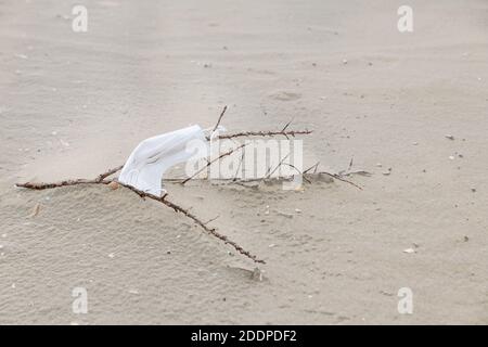 Eine Gesichtsmaske zum Schutz während der Covid-19 Pandemie wird am Strand zurückgelassen und verursacht Umweltverschmutzung. Stockfoto