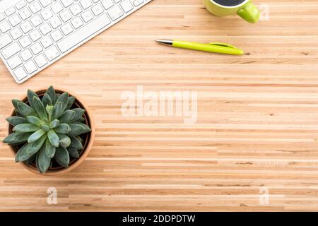 Holzschreibtisch mit Computertastatur, Kaffeetasse, Topfpflanze, Kugelschreiber und Kopierraum, Blick in den hohen Winkel Stockfoto