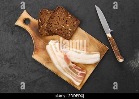 Von oben aus gesehen zwei Scheiben Speck und braunes Brot auf einem Holzschneidebrett Stockfoto