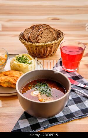 Rustikales Abendessen - Hähnchenfilet in Panade, Kartoffelpüree und Gurkenkohl mit Salzwürzesuppe, braunem Brot und einem Glas Preiselbeersaft Stockfoto