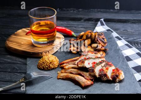 Gebratenes Fleisch serviert mit gebratenen Pilzen und einer Scheibe Speck, Senf und einem Glas Bourbon Stockfoto