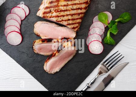 Gegrilltes Schweinefilet in Scheiben mit frischen Tomaten und Radish mit einem Glas Rotwein serviert. Stockfoto