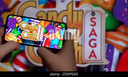 Nova Lima, Brasilien - November 2020: Hände halten ein Smartphone mit dem CANDY CRUSH SAGA Spiel im HINTERGRUND des großen Bildschirms Stockfoto