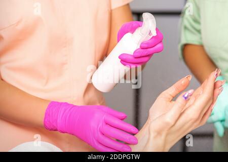 Kosmetikerin in Gummi Schutzhandschuhe desinfiziert Hände der Frau mit Antiseptisches Spray in einem Schönheitssalon Stockfoto