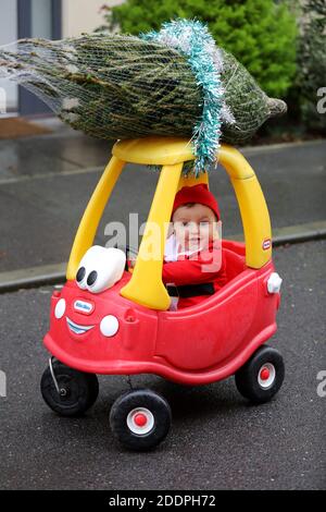 Niedlicher einjähriger Junge namens Oscar, der als Weihnachtsmann gekleidet war und einen kleinen Weihnachtsbaum auf seinem klassischen roten Tikes-Auto in Großbritannien ablieferte. Stockfoto