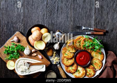 Kartoffelpfannkuchen mit Quark mit Knoblauch, Petersilie, serviert mit Ketchup auf einem Teller auf einem Holzhintergrund, Draufsicht, Nahaufnahme Stockfoto