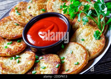 Kartoffelpfannkuchen mit Quark mit Knoblauch, Petersilie, serviert mit Ketchup auf einem Teller auf einem Holzhintergrund, Draufsicht, Nahaufnahme Stockfoto