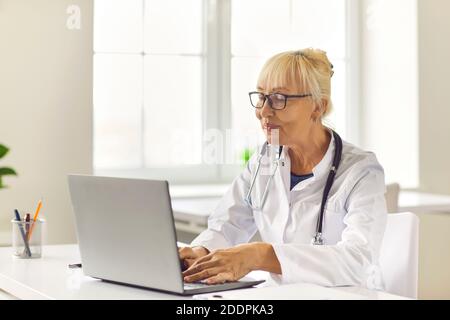Lächelnde leitende Ärztin führt online per Laptop mit dem Patienten Kontakt auf. Stockfoto