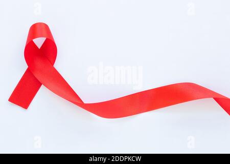 Rotes Band auf weißem Stoffhintergrund mit Kopierraum, Symbol für die Solidarität von Menschen, die mit HIV/AIDS leben, und für das Bewusstsein und die Prävention Stockfoto