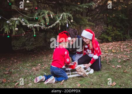 Vater und zwei Töchter öffnen Geschenke Boxen in der Nähe Weihnachtsbaum im Freien im Hof des Hauses. Frohe Weihnachten und frohe Feiertage Stockfoto