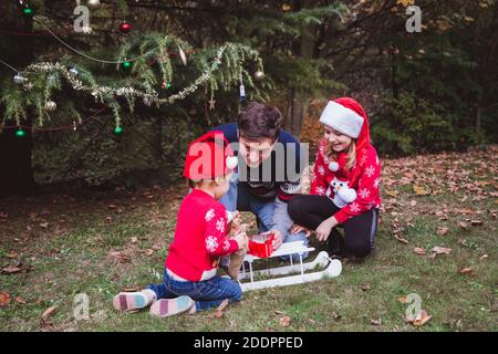 Vater und zwei Töchter öffnen Geschenke Boxen in der Nähe Weihnachtsbaum im Freien im Hof des Hauses. Frohe Weihnachten und frohe Feiertage Stockfoto