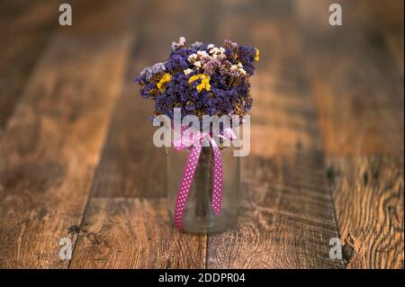 Ein Bouquet von getrockneten Blumen, Limonium sinuatum, Wellenblatt Meer Lavendel, Statice, Notch Blatt Sumpf Rosmarin, Meer rosa in einem Glas, rosa Band, Holzboden Stockfoto