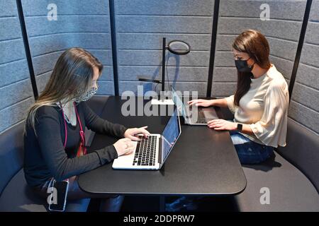 Themenbild Coworking Space: Zwei junge Frauen arbeiten am 22. November 2020 in einem Coworking-Büro an ihren Laptops. Coworking ist eine Entwicklung im Bereich der "neuen Arbeitsformen". Freiberufler, kleinere Startups oder digitale Nomaden arbeiten in meist größeren, relativ offenen Räumen und können so voneinander profitieren. Sie arbeiten entweder selbstständig in verschiedenen Unternehmen und Projekten oder entwickeln gemeinsam mit anderen Mitarbeitern Projekte. MODELL FREIGEGEBEN! Weltweite Nutzung Stockfoto