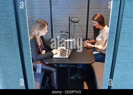 Themenbild Coworking Space: Zwei junge Frauen arbeiten am 22. November 2020 in einem Coworking-Büro an ihren Laptops. Coworking ist eine Entwicklung im Bereich der "neuen Arbeitsformen". Freiberufler, kleinere Startups oder digitale Nomaden arbeiten in meist größeren, relativ offenen Räumen und können so voneinander profitieren. Sie arbeiten entweder selbstständig in verschiedenen Unternehmen und Projekten oder entwickeln gemeinsam mit anderen Mitarbeitern Projekte. MODELL FREIGEGEBEN! Weltweite Nutzung Stockfoto