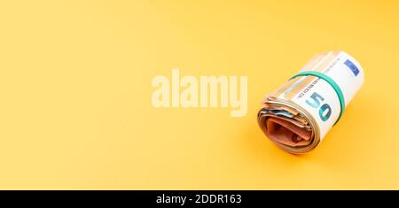 Große Ansicht der großen Geldrolle der Euro-Banknoten Mit Gummiband auf orangefarbenem Hintergrund Stockfoto