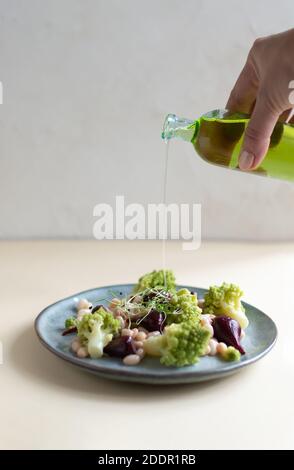 Salat aus Mini-Rüben, Romanesco-Kohl, weißen Bohnen und eingiessenden Olivenöl auf einem grauen Teller auf hellem Hintergrund. Gesunde Ernährung Konzept. Selektiver Fokus Stockfoto