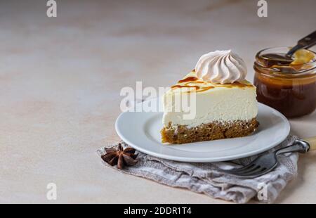 Stück Karotten-Vanille-Käsekuchen mit gesalzenem Karamell-Belag und Baiser auf einer weißen Keramikplatte, heller Betonhintergrund. Selektiver Fokus. Stockfoto