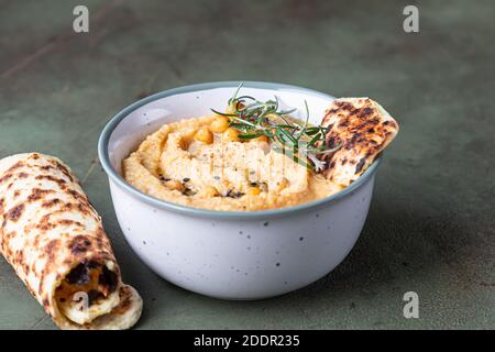 Klassischer Hummus mit Rosmarin, Fladenbrot, gekochten Kichererbsen und Olivenöl, Hintergrund aus grünem Stein. Traditioneller Nahost-Snack. Selektiver Fokus. Stockfoto
