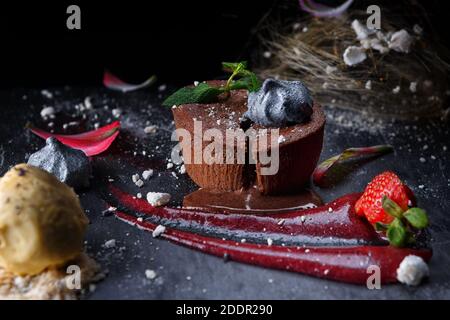 Schokoladenfondant auf schwarzem Hintergrund mit Erdbeeren und Blumen Stockfoto