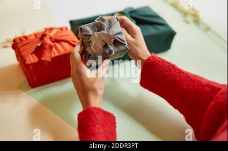 Junge Frau hält ein Zero Waste Geschenk in traditionellen japanischen Furoshiki-Stil verpackt. Weihnachtsdekorationen, mittlere Nahaufnahme Stockfoto