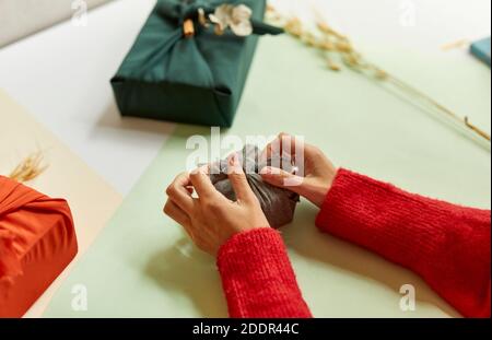 Furoshiki Japanisches Geschenk von einer Frau in roten Pullover gewickelt, Tutorial. Herbst handgewickeltes Geschenk im traditionellen Furoshiki-Stil Stockfoto