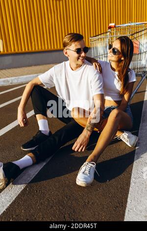 Ein junger Mann und ein Mädchen posieren auf dem Asphalt, in der Stadt gegen eine gelbe Wand. Das Konzept des Shoppings Stockfoto