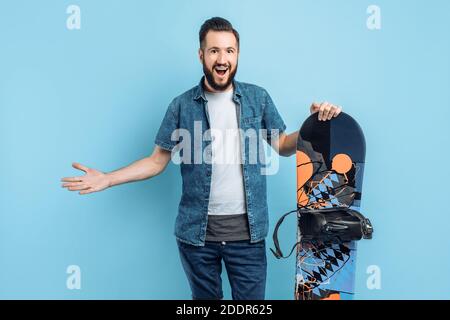 Glücklich attraktiver Mann mit einem Bart trägt Shorts und ein shirt mit einem Snowboard isoliert auf einem blauen Hintergrund Stockfoto