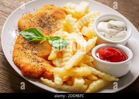 Teller mit Hühnerschnitzel und pommes auf Holztisch Stockfoto