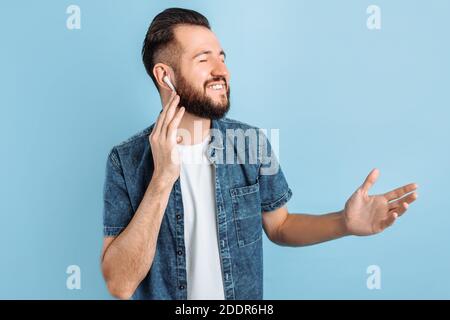 Auf der Seite, ein Porträt eines lächelnden jungen Mannes Musik oder Radio hören verwendet moderne kabellose Kopfhörer, stehen auf einem isolierten blauen Hintergrund Stockfoto