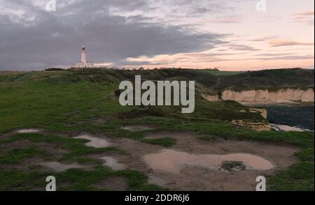 Zerklüftete Küste mit Regenpfützen, Kreidefelsen und Leuchtturm, mit warmem Glanz des Himmels bei Sonnenaufgang in Flamborough Head, Yorkshire, Großbritannien. Stockfoto