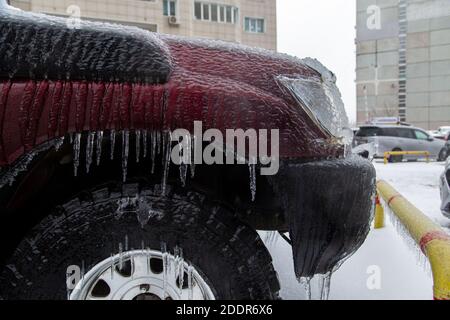 Der rote Kotflügel, das Rad und der Stoßfänger des SUV sind durch den Regen im Winter sehr eisig. Eiszapfen hängen herunter. Stockfoto