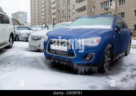 Der blaue SUV und andere Autos stehen in der Stadt gefroren und eisig vom Regen im Winter. Durch Eis blockiert. Stockfoto