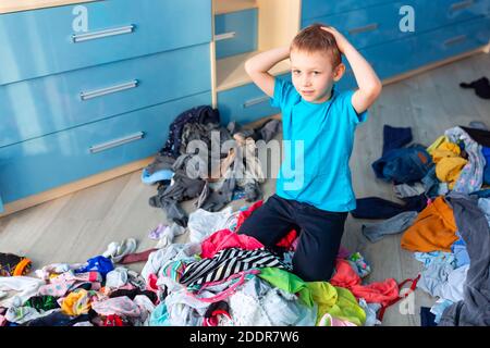 Der kleine Junge verzweifelte mit dem Chaos in seiner Kleidung in seinem Schlafzimmer. Stockfoto