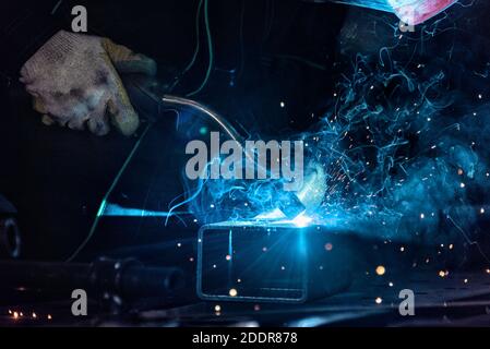 Nahaufnahme des MIG-Schweißbrenners auf Metall mit Funken Und Dämpfe, die vom blauen Licht des Hochs erleuchtet werden Temperaturflamme Stockfoto