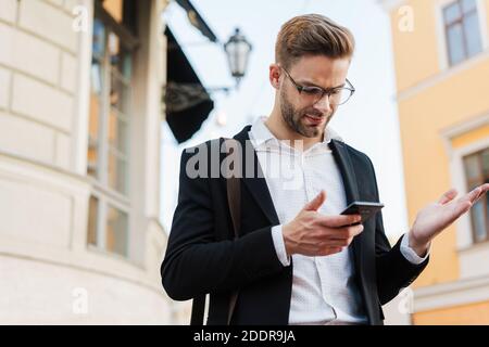 Gut aussehend verwirrt Geschäftsmann in Brillen mit Handy in der Stadt Straße Stockfoto