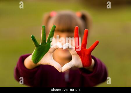 Herz Form von Kindern handbemalt in italien Flagge Farben, Kinder Körpersprache, Kinder Liebe Konzept. Herz Hand auf Natur Sonnenuntergang Bokeh Hintergrund Stockfoto