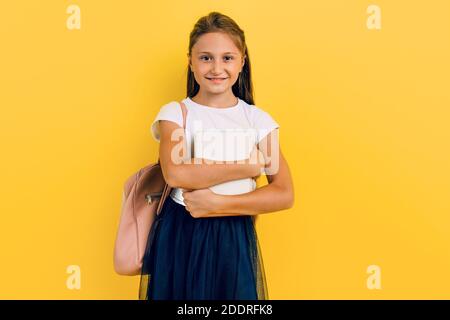 Ein Teenager in Schulkleidung mit Rucksack und Büchern. Zielstrebig und fleißig. Stilvolle schöne Schulmädchen posiert auf einem gelben Hintergrund Stockfoto