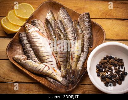 Draufsicht frischer Fisch auf einem hölzernen quadratischen Braun Teller auf dem Holzhintergrund mit Zitrone und Gewürzen verziert In der weißen Tasse Stockfoto