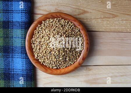 Flache Ansicht einer Holzschüssel voller malzter Gerstenkörner, einer Hauptzutat in der Bierbrauerei und Whisky-Destillation. Mit blauem schottischem Tartan-Tischtuch Stockfoto