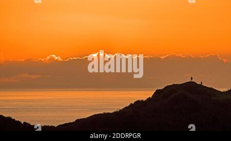 Langland Bay, Swansea, Großbritannien. November 2020. Menschen, die über den Langland Bay Golfplatz wandern, halten an, um den Sonnenuntergang hinter den Wolken am Gower Küstenhorizont in der Nähe von Swansea am Nachmittag am Ende eines sonnigen, aber kalten Herbsttages zu beobachten. Quelle: Phil Rees/Alamy Live News Stockfoto