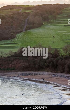 Langland Bay, Swansea, Großbritannien. November 2020. Schwimmer trotzen dem kühlen Meer in der Langland Bay in der Nähe von Swansea an diesem Nachmittag, während Golfer am Ende eines sonnigen, aber kalten Nachmittags den frostigen 17. Fairway im Langland Bay Golf Club entlang laufen. Quelle: Phil Rees/Alamy Live News Stockfoto