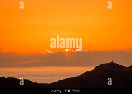 Langland Bay, Swansea, Großbritannien. November 2020. Menschen, die über den Langland Bay Golfplatz wandern, halten an, um den Sonnenuntergang hinter den Wolken am Gower Küstenhorizont in der Nähe von Swansea am Nachmittag am Ende eines sonnigen, aber kalten Herbsttages zu beobachten. Quelle: Phil Rees/Alamy Live News Stockfoto