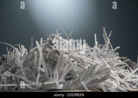 Nahaufnahme mit optischer Tiefe von weißen Papierblättern, die vor einer blauen Wand in Streifen geschnitten wurden. Stockfoto